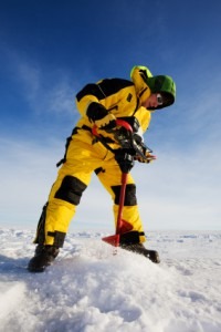 man drills hole in ice with auger 